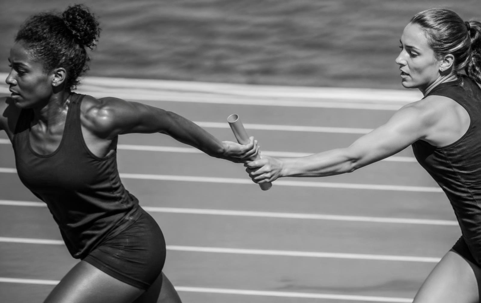 Relay runners mid baton handoff on the track